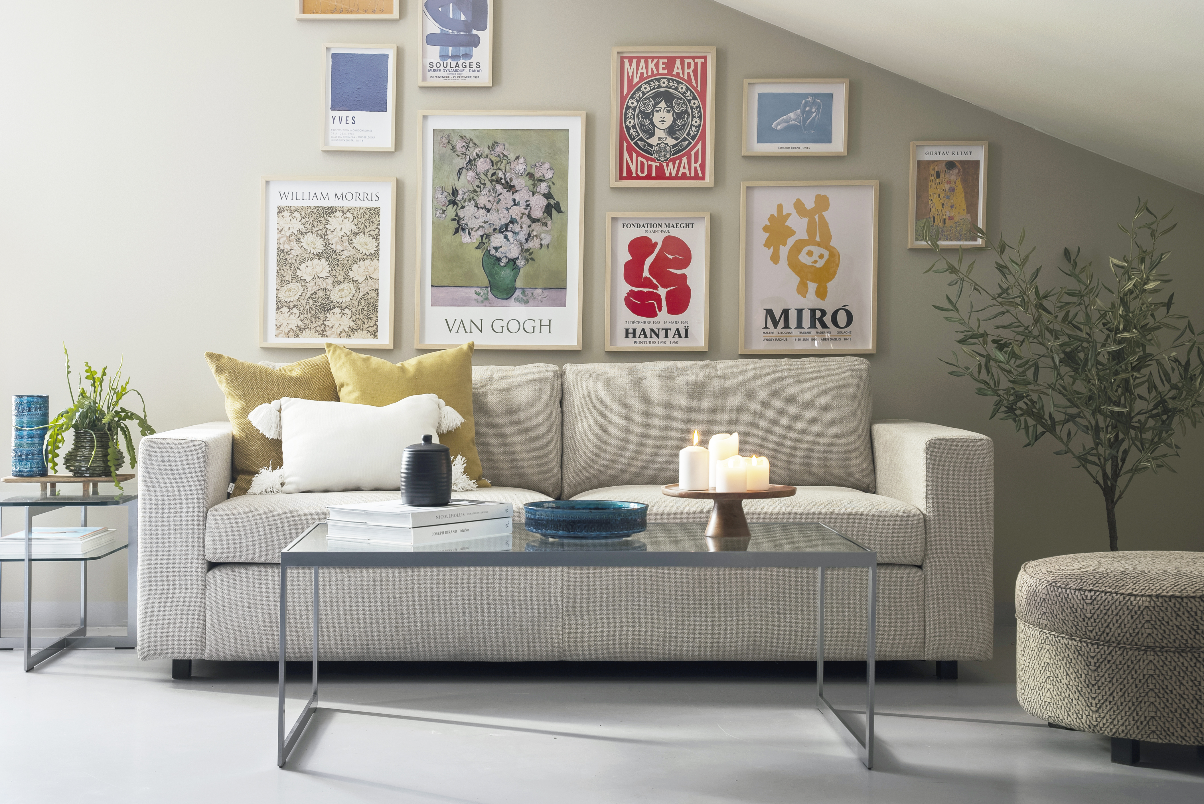 Soffan Djursholm från englesson i ljust tyg under en tavelvägg.