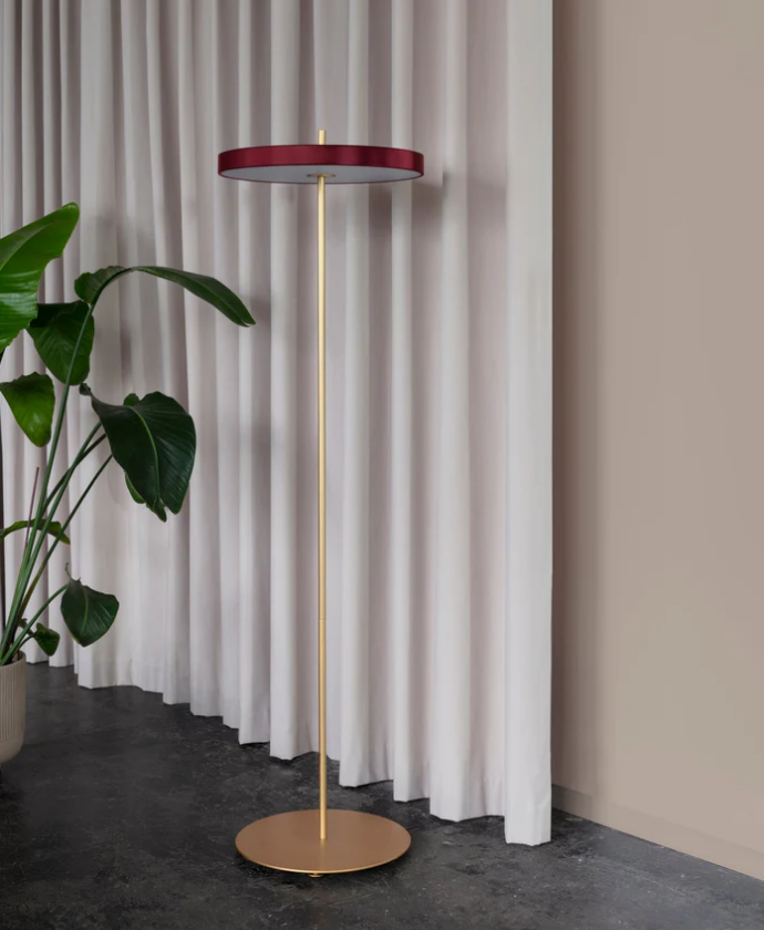 Asteria golvlampa i en inbjudande röd nyans mot mässingsdetaljerna.